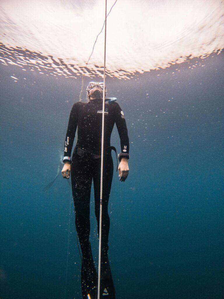 Freediver in wetsuit ascending underwater in Lombok, Indonesia, showcasing diving adventure.