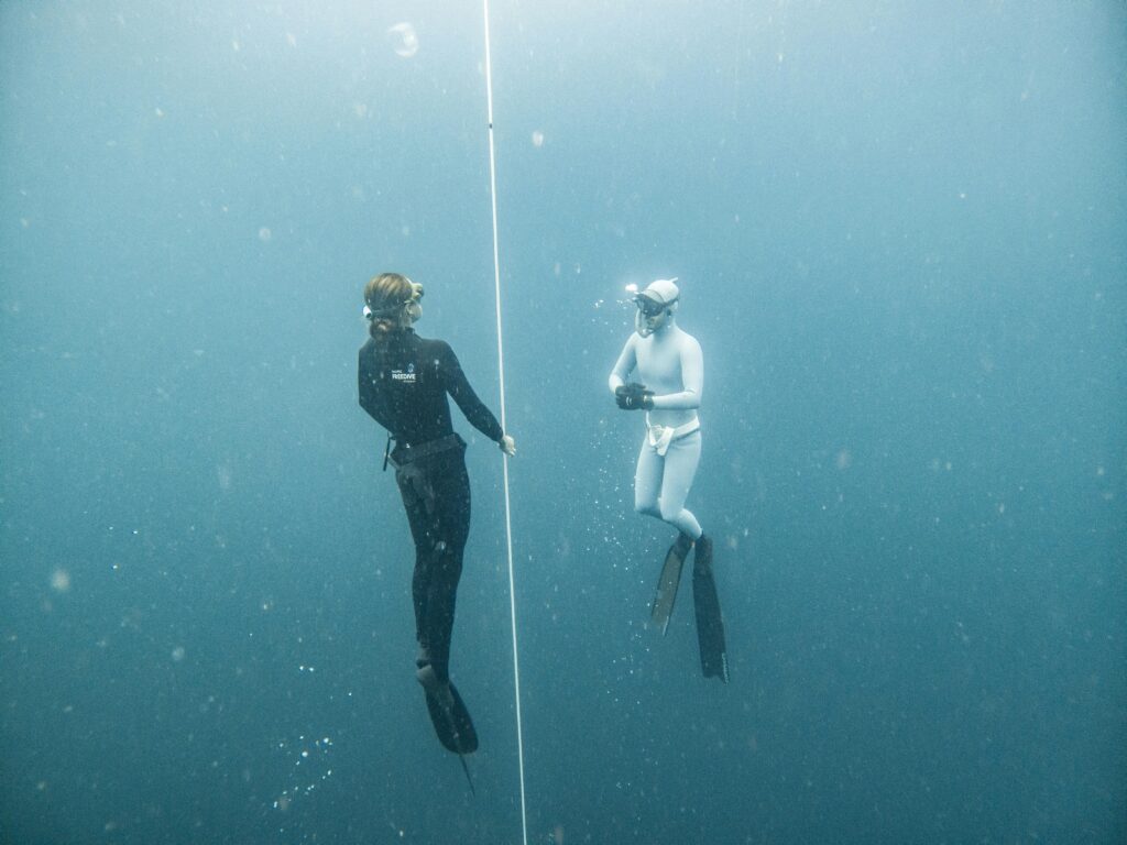 Two freedivers explore deep blue waters in Lombok, Indonesia, using guide rope for orientation.